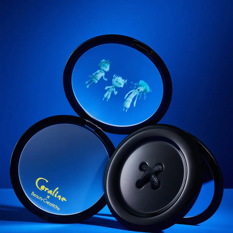 Beauty Creations Coraline Button Eyes Compact Mirror featuring a button design on a vibrant blue background.